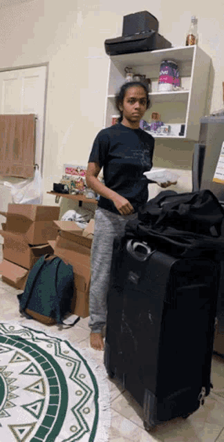 a woman standing next to a suitcase in a room with boxes on the floor and a can of ovo on the shelf
