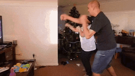 two men are dancing in a living room in front of a christmas tree