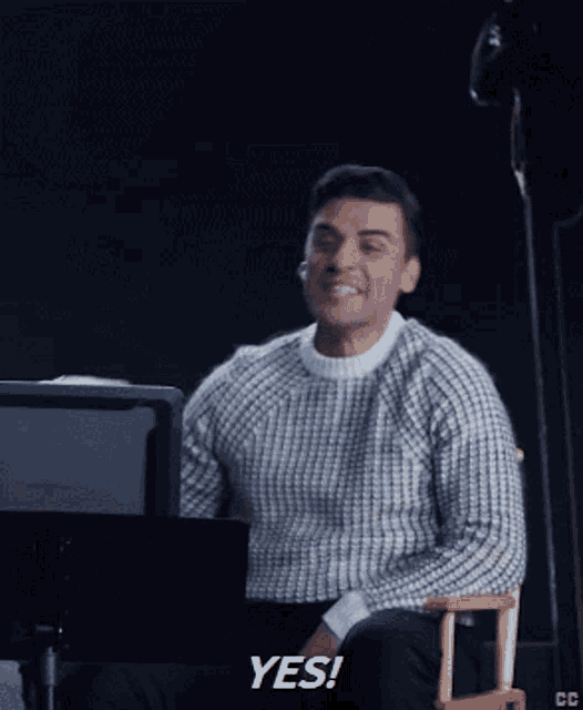 a man in a striped sweater is sitting in front of a computer and says yes