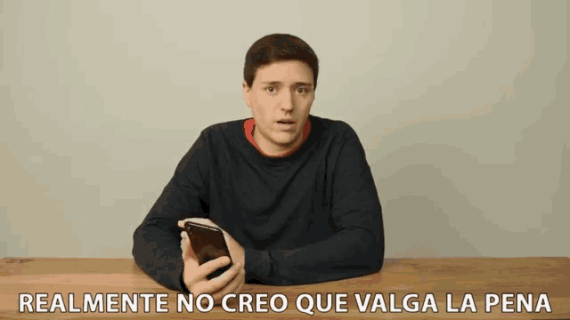 a man sitting at a table holding a cell phone with the words " realmente no creo que valga la pena " written below him
