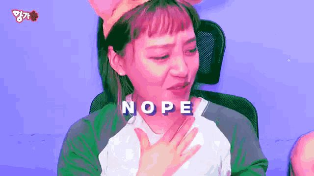 a girl with pink hair is sitting in a chair with her hand on her chest and the word nope is written above her .