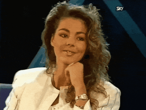 a woman with a watch on her wrist looks at the camera with the sky logo behind her