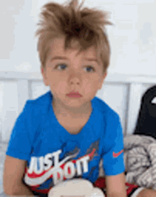 a young boy wearing a blue nike just do it shirt is sitting on a bed .