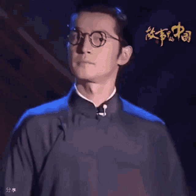 a man wearing glasses is standing in front of a sign that says ' a ' on it