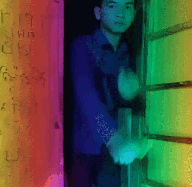 a man in a blue shirt stands in front of a wall with graffiti on it that says " i his on "