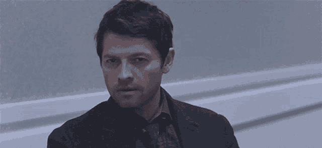 a man in a suit looks at the camera in a dark room