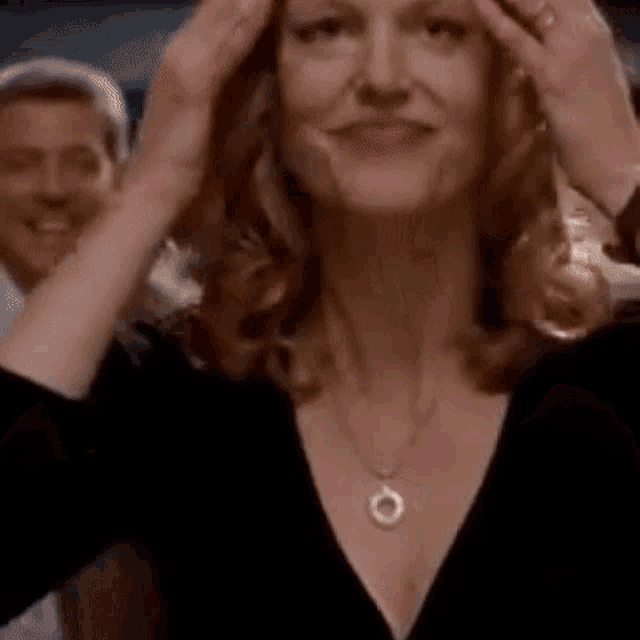 a woman wearing a necklace and a black shirt is holding her head .