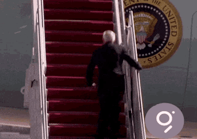 a man climbs the stairs of an airplane with the seal of the united states behind him