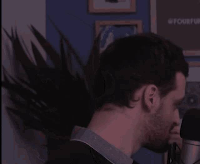 a man stands in front of a microphone with his hair blowing in the wind and a sign on the wall that says @forwar
