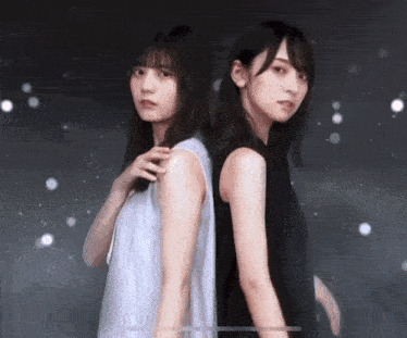 two women are standing back to back in front of a dark background .