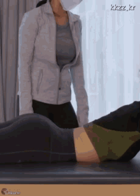 a woman wearing a mask is standing next to a woman laying on a massage table .
