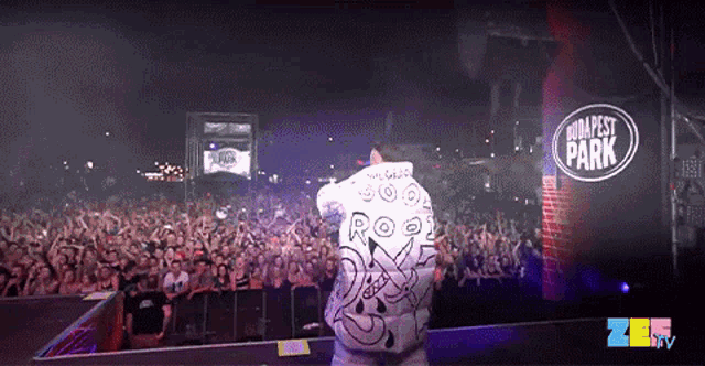 a man stands on a stage in front of a crowd with a sign that says ' budapest park ' on it