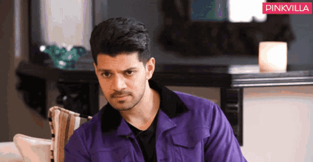 a man in a purple jacket is sitting on a couch