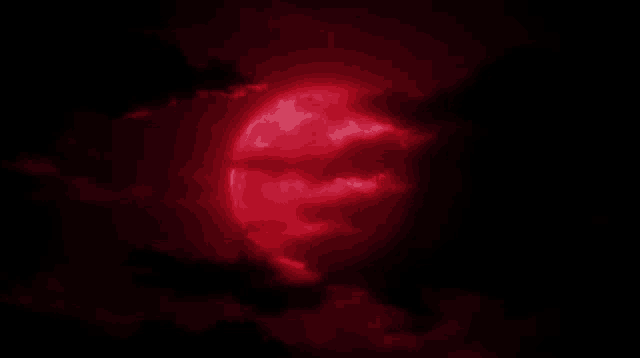 a red moon is visible through the clouds in the night sky