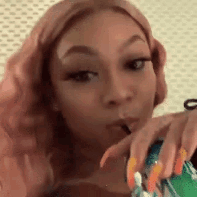 a woman with pink hair and long nails is drinking from a straw .