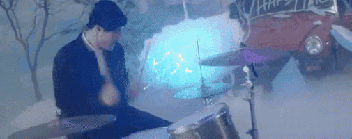 a man is playing drums in front of a red car in the snow .
