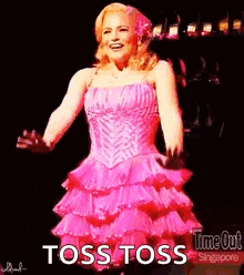 a woman in a pink dress is standing on a stage and says toss toss .