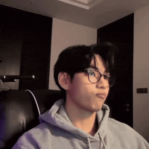 a young man wearing glasses and a grey hoodie is sitting in a chair