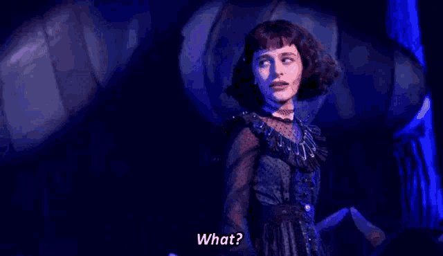 a woman in a black dress is standing on a stage in front of a monster and saying what .