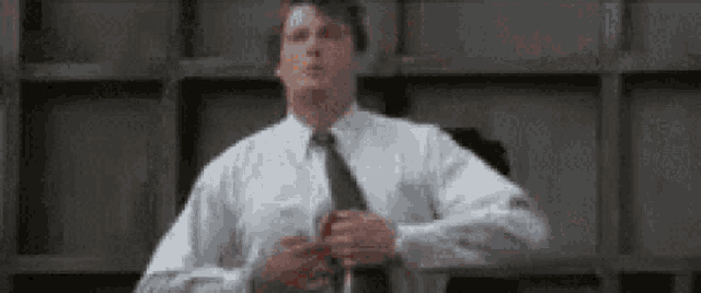 a man in a white shirt and tie is adjusting his tie in front of a wall .