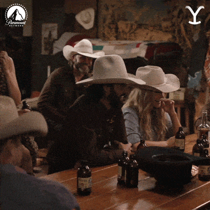 a group of people wearing cowboy hats sit at a table with bottles of beer and a paramount logo in the background