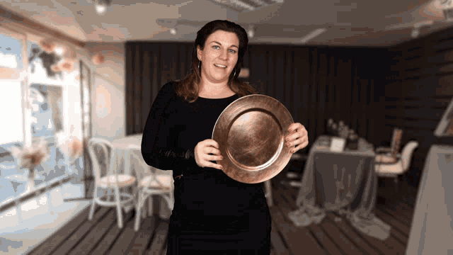 a woman in a black shirt is holding a copper plate