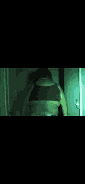 a woman in a black bra is standing in a dark room with a green light behind her .