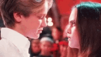 a boy and a girl are looking into each other 's eyes in a crowded room .