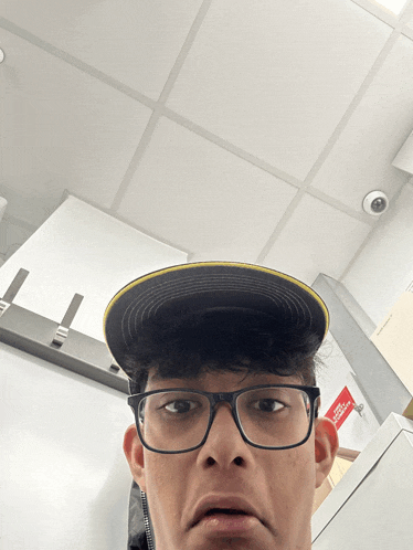 a man wearing glasses and a hat has a red sign on the wall that says fire escape