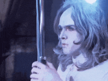 a man with long hair and white paint on his face is holding a pole