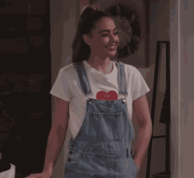 a woman wearing overalls and a white t-shirt with a red heart that says i love you