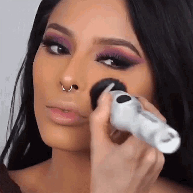 a woman with a nose ring is getting her makeup applied