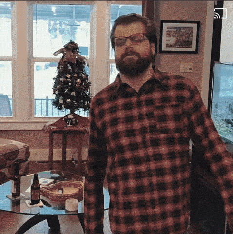 a man wearing glasses and a plaid shirt is standing in front of a christmas tree