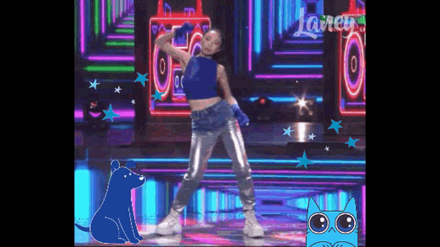 a woman in a blue top and silver pants is dancing on a stage next to a blue dog