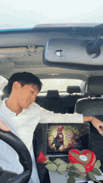 a man sitting in a car next to a laptop and a heart shaped valentine 's day box