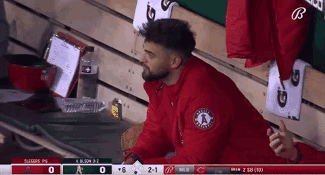 a man in a red jacket sits in the dugout during a baseball game between the angels and the cubs