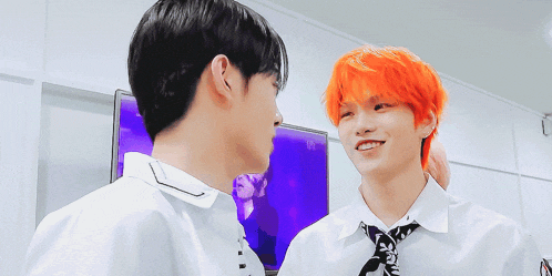 a man with orange hair is smiling next to another man with black hair .