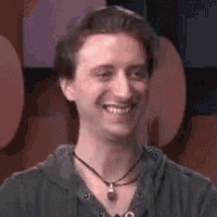 a man wearing a hoodie and a necklace is smiling and looking at the camera .