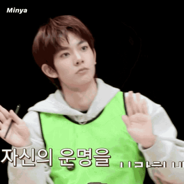 a young man wearing a green vest and a white hoodie says minya on the bottom