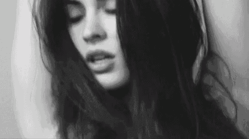 a black and white photo of a woman with her eyes closed and her hair blowing in the wind .