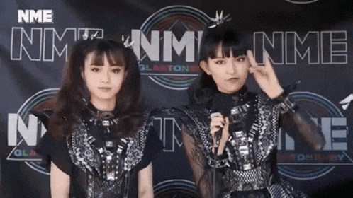 two girls are standing next to each other in front of a nme sign .