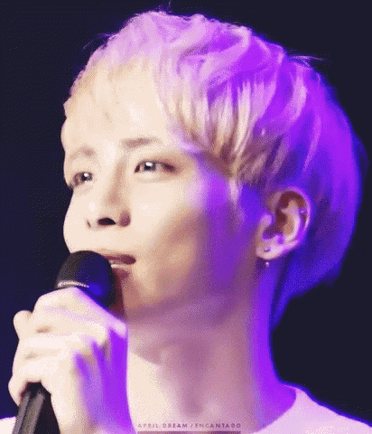 a young man is singing into a microphone in front of a purple light .