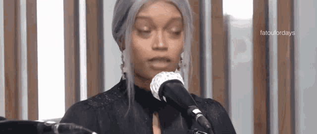 a woman is singing into a microphone while wearing a wig and earrings .