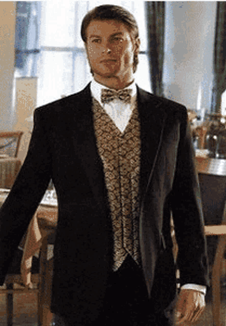 a man in a tuxedo and bow tie stands in a room