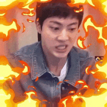 a man in a denim jacket is surrounded by fire and making a funny face .