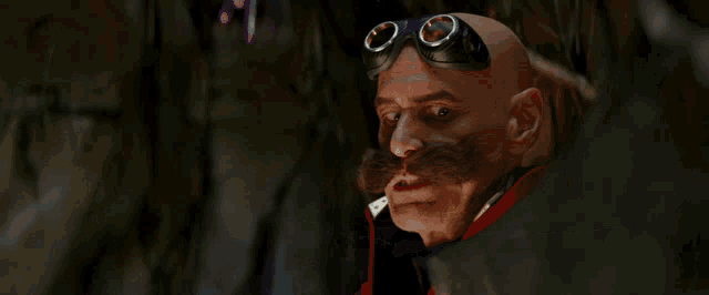 a bald man with a mustache wearing goggles looks at something