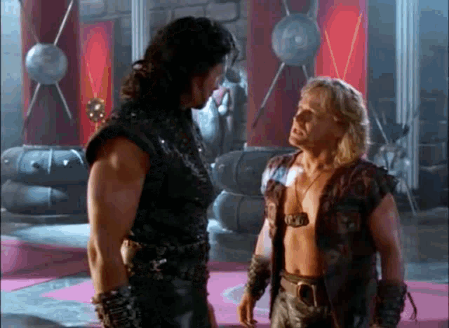 two men are standing next to each other in a room with shields in the background