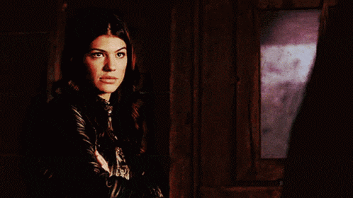 a woman in a black leather jacket stands in front of a window