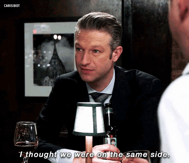 a man in a suit and tie says " i thought we were on the same side " in front of a lamp