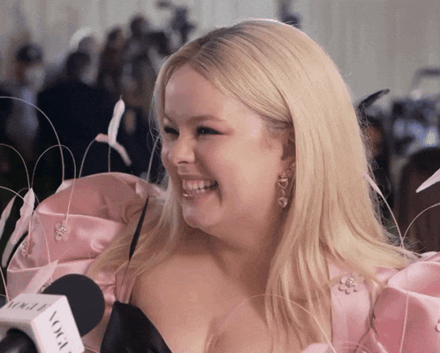 a woman in a pink dress is smiling in front of a microphone that says vogue on it